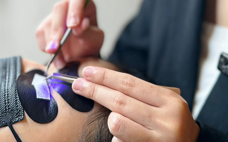 Beautician using tweezers to apply LED eyelash extensions carefully.